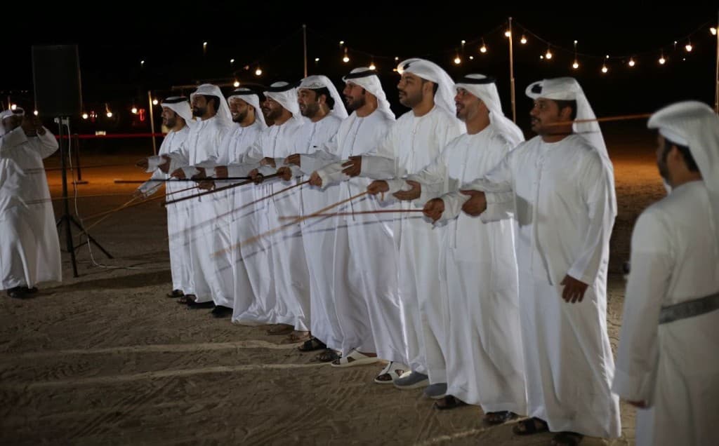 Long line of Al Ayyala performers under festoon lights at a night event in Abu Dhabi