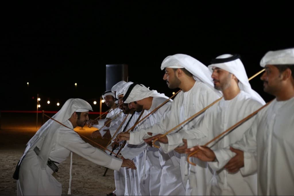 Al Ayyala dancers in kandura performing on sand at night in Abu Dhabi