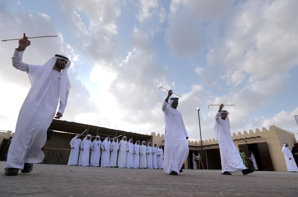 Al Ayyala stick dance in a paved heritage courtyard with fort-style walls in Abu Dhabi