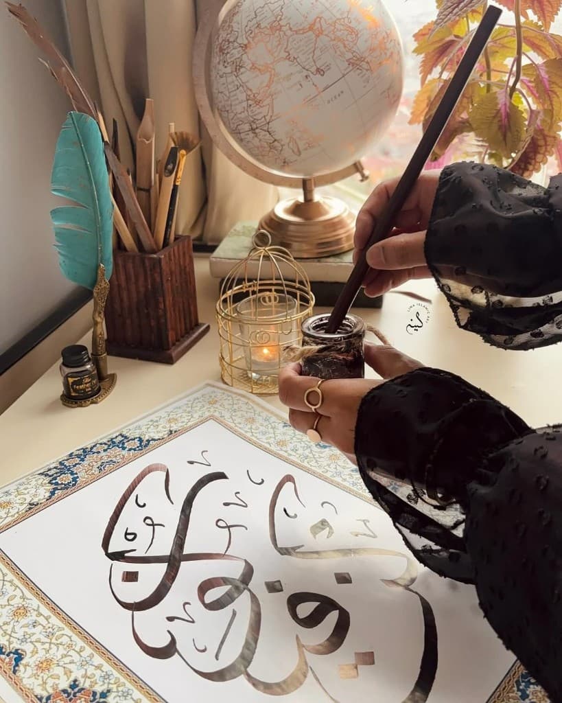 Calligrapher dipping a qalam into ink beside a finished Arabic piece in Sharjah