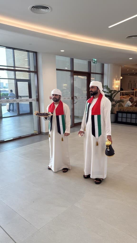 Two men in kandura serving dates and Arabic coffee in a bright indoor hall in Abu Dhabi