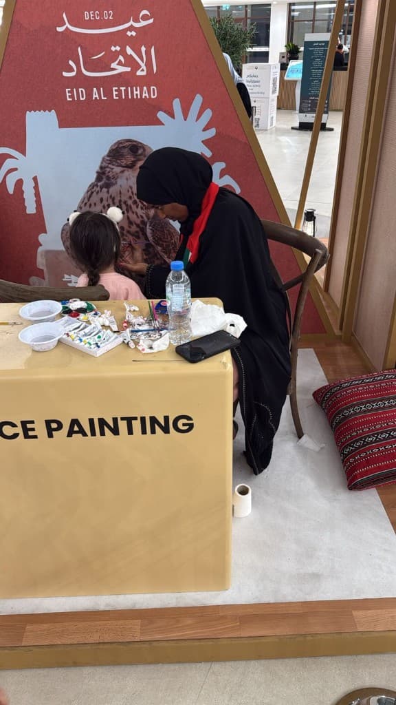 Face painter working on a child at an Eid Al Etihad station with Dec. 02 branding in Abu Dhabi