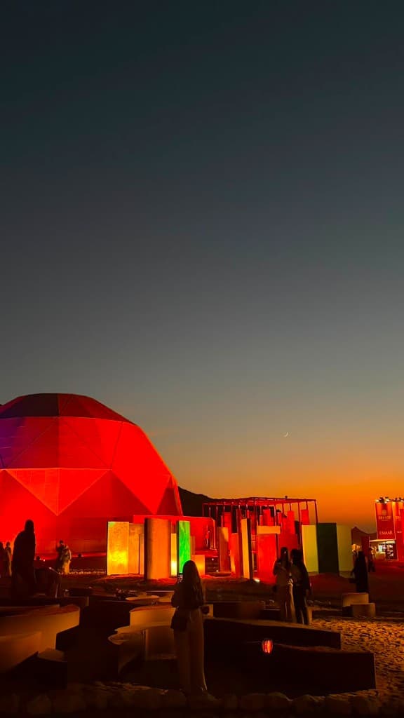 Geodesic dome and coloured light walls on sand at dusk with Emaar signage in Dubai