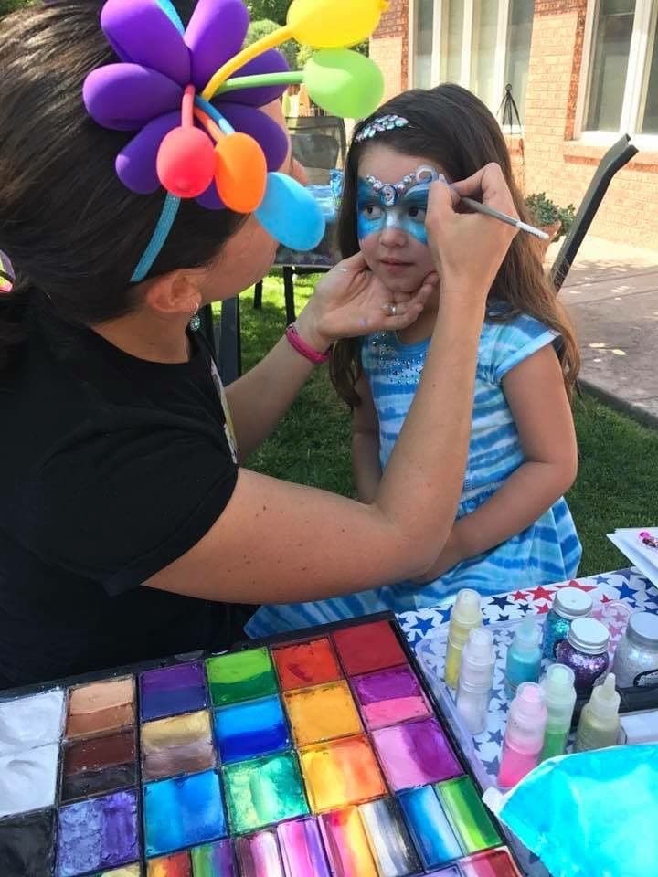 Face painter applying a blue crown design to a child at an outdoor event in Sharjah