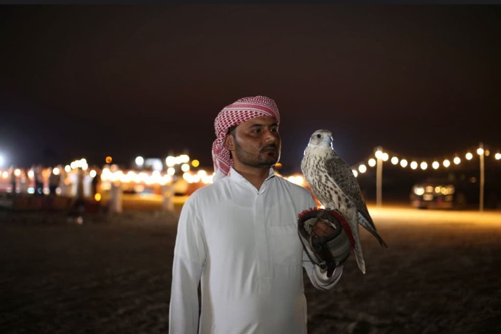 Man in kandura holding a falcon on a leather glove at a night event in Abu Dhabi