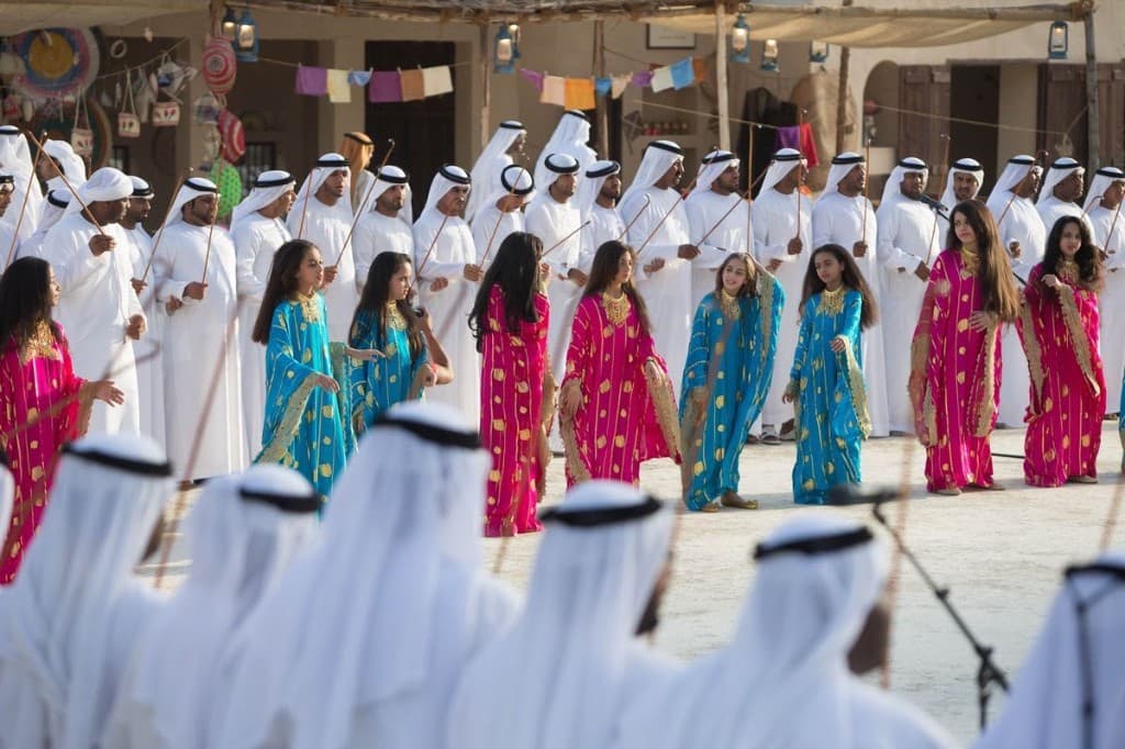 Young dancers in pink and turquoise dresses performing with Al Ayyala men in an Abu Dhabi heritage courtyard
