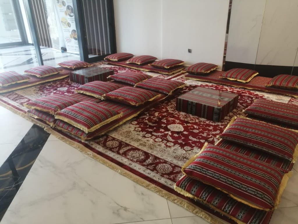 Indoor Sadu majlis with red striped floor cushions and low tables in Abu Dhabi