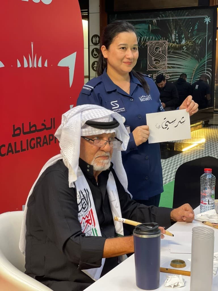 Calligrapher in kandura writing Arabic script for a guest at an Abu Dhabi event