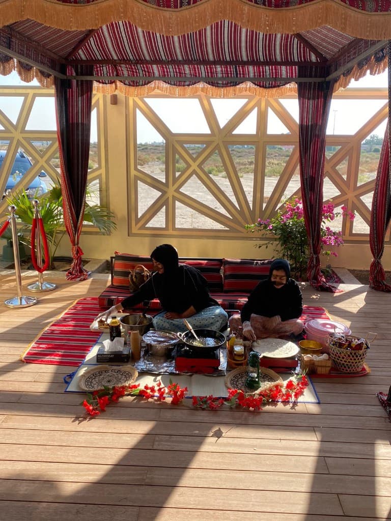 Two women in abaya cooking raqaq bread and pan dishes under a Sadu canopy in Abu Dhabi
