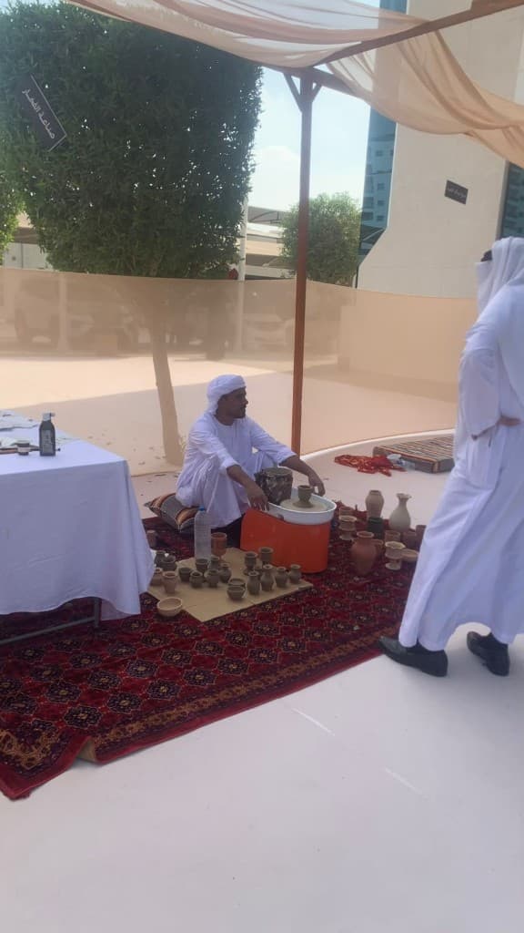 Man in kandura shaping clay on a pottery wheel under a canopy in Al Ain