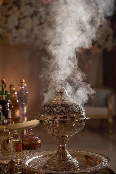 Silver mabkhara releasing bakhoor smoke beside attar bottles at an Abu Dhabi event