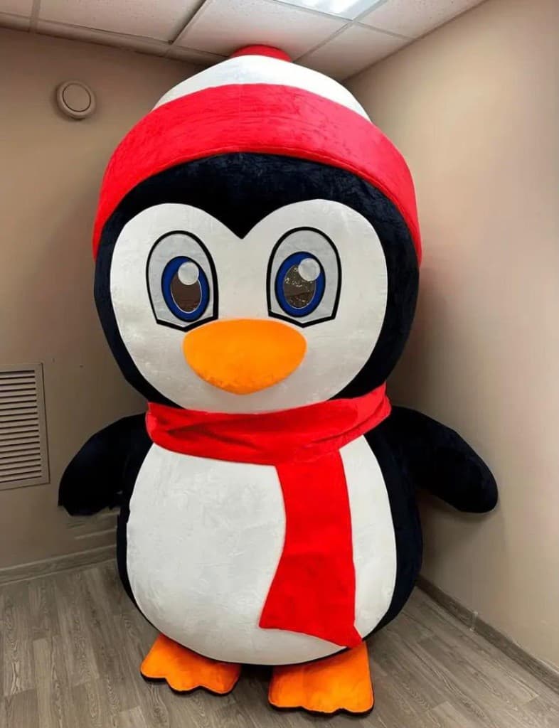 Penguin mascot in a red scarf standing indoors for a Dubai festive event