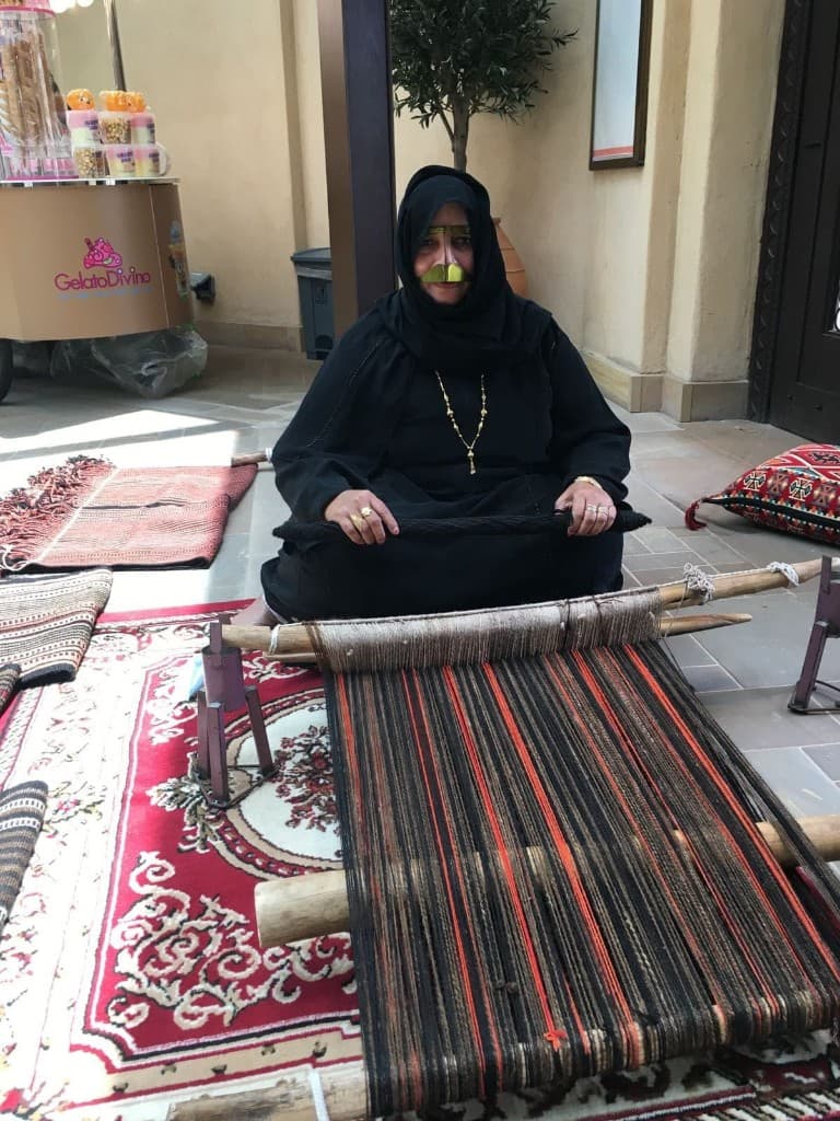 Woman in abaya and gold burqa weaving Sadu on a ground loom in Abu Dhabi